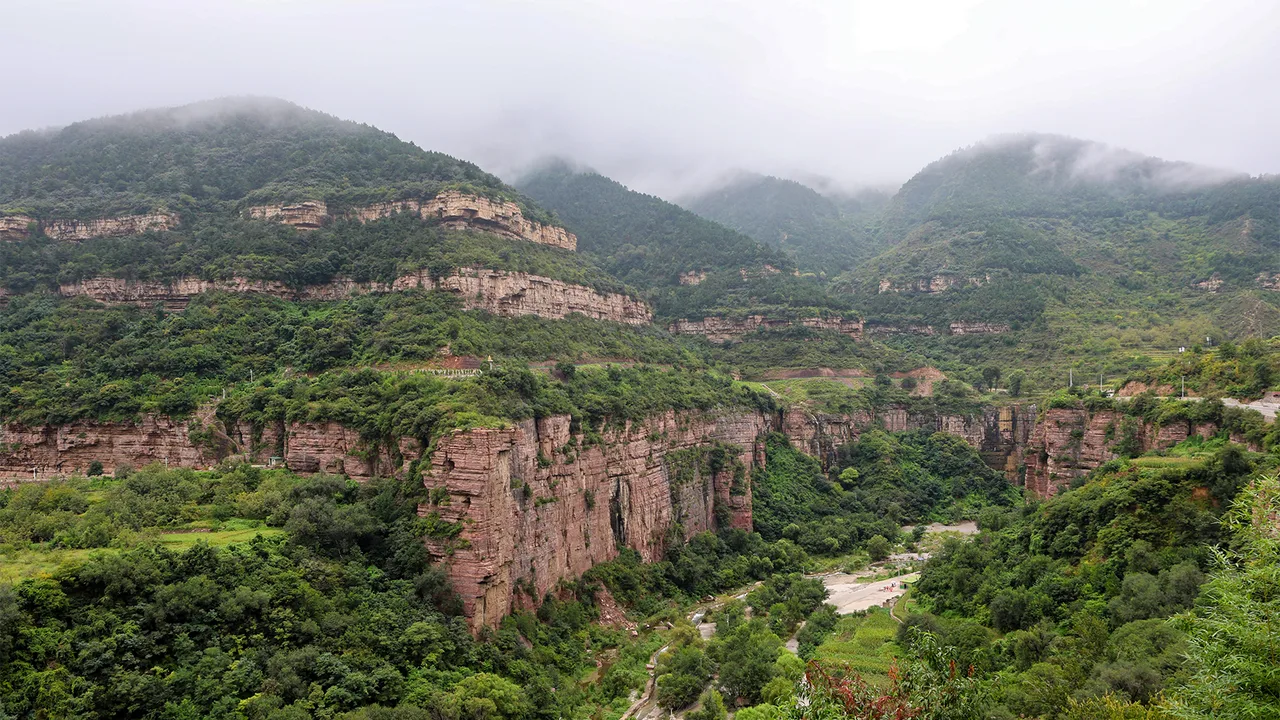 Layered red cliffs and green forested slopes of the Taihang Grand Canyon in Huguan county, Changzhi, under low cloud.