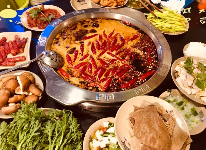 A boiling metal pot partitioned into nine squares, filled with dark red broth, dried red chilis, and Sichuan peppercorns.