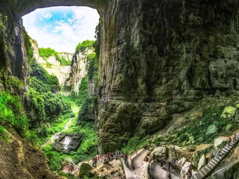 A view of the Tianlong Outpost nestled between towering karst cliffs under a massive natural stone bridge in Wulong.