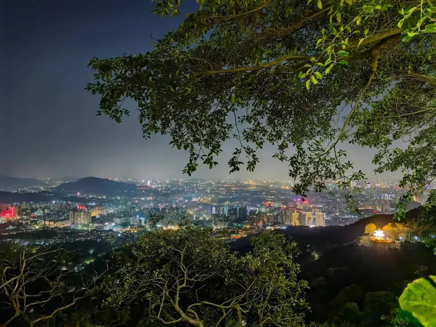 A misty view of forested ridges on Baiyun Mountain with Guangzhou buildings in the far distance.