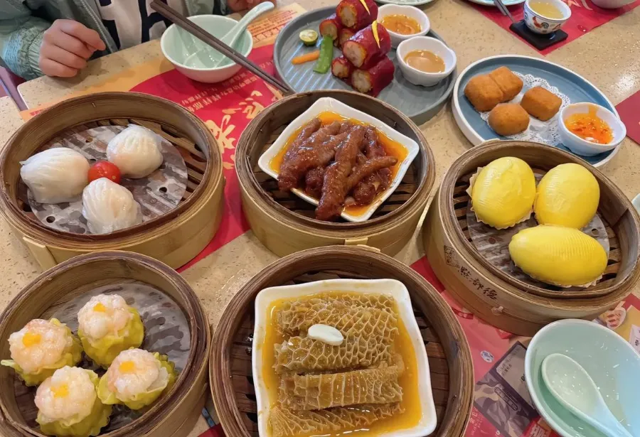 A table filled with bamboo steamers of dim sum, including shrimp dumplings and buns, next to a teapot at a traditional teahouse in Guangzhou.