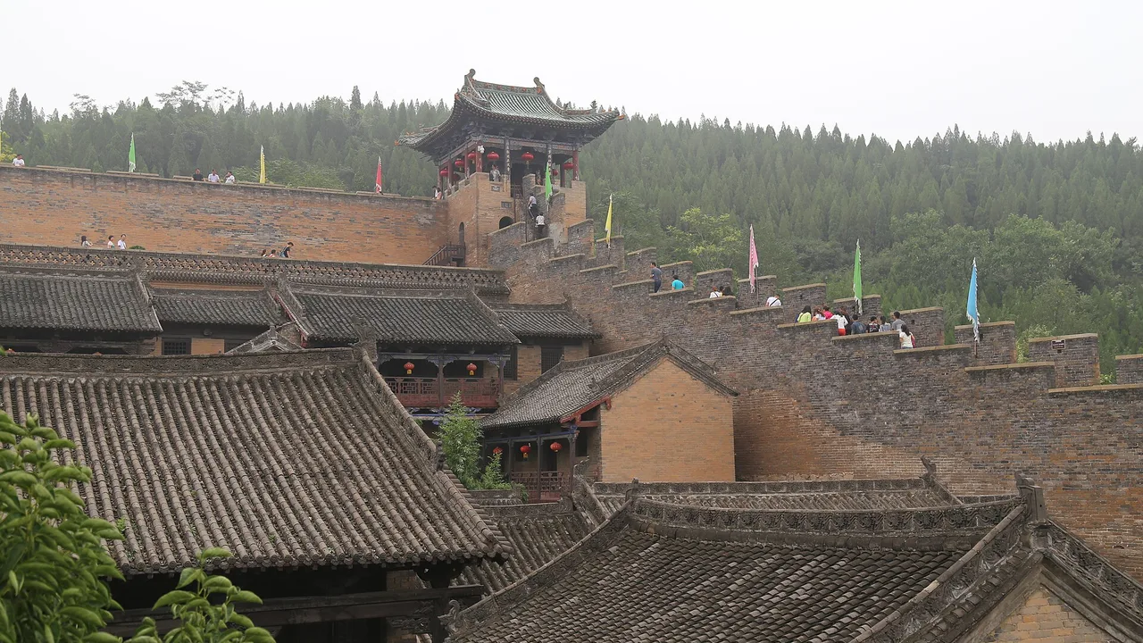 Tiled courtyard roofs of Huangcheng Xiangfu spreading toward a pavilion and wooded hills.
