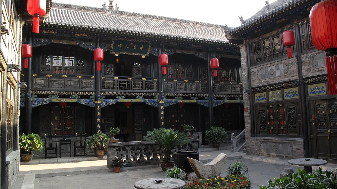 A Pingyao courtyard inn with dark carved timber facades, red lanterns and potted plants.