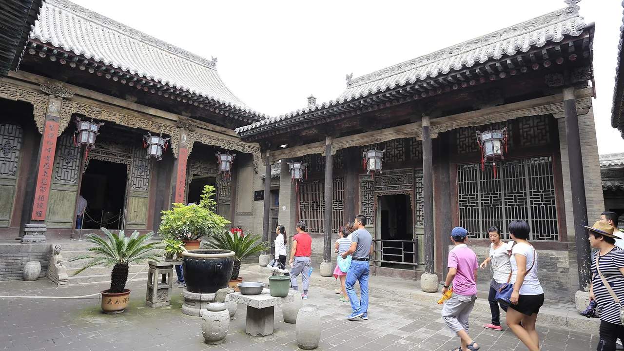 Visitors in a paved courtyard between carved timber halls at the Wang Family Courtyard in Jingsheng, Lingshi.