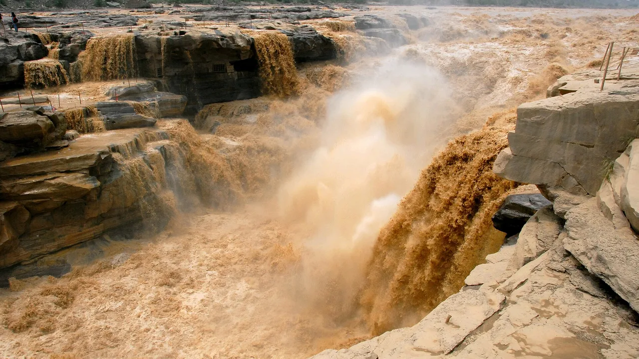 Brown Yellow River water pouring into the rock trough at Hukou Waterfall, with spray rising.