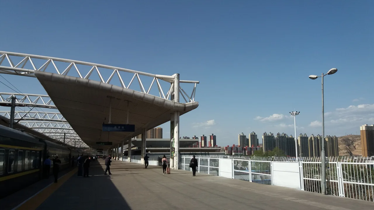 Platform and canopy at Lüliang Railway Station in Lishi on a clear day, with a train waiting at the platform.