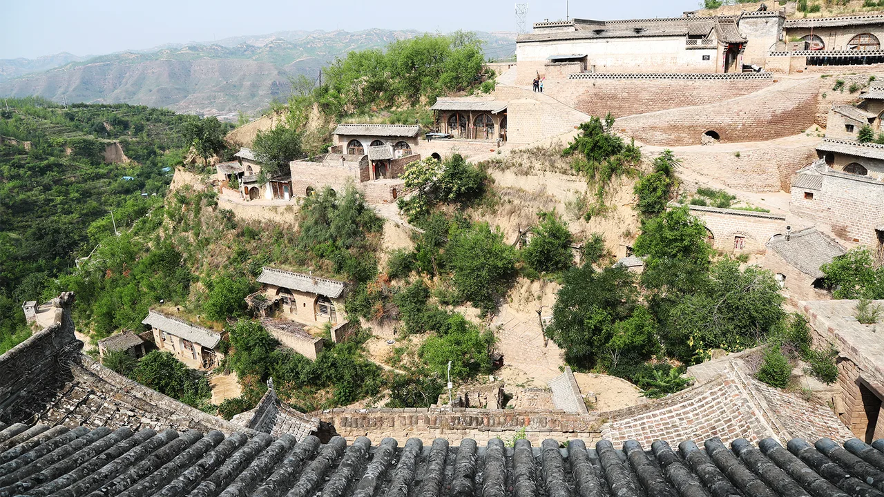 Cave houses and courtyards scattered down a loess hillside at Lijiashan, with green terraces and the Lüliang hills behind.