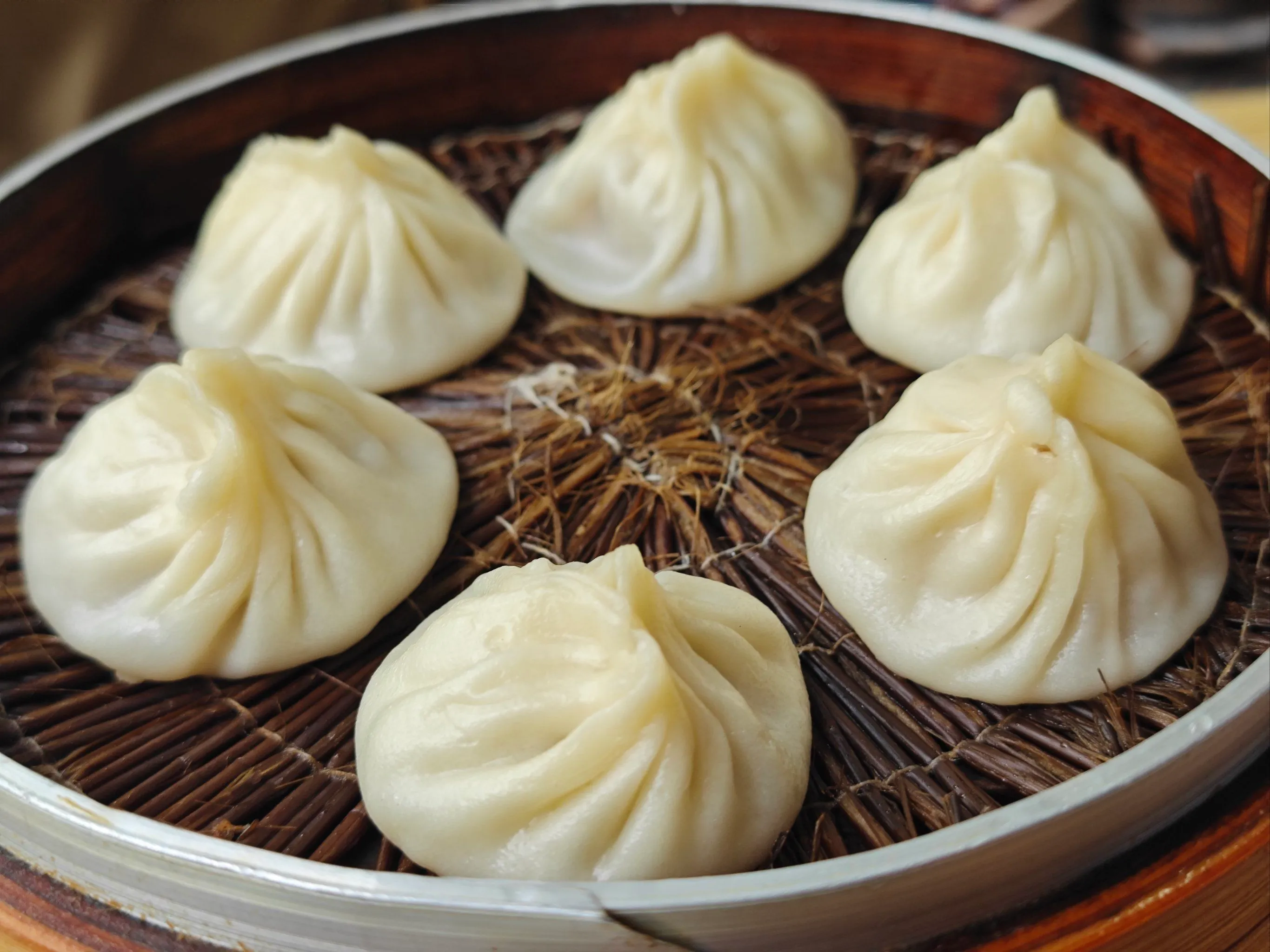 A bamboo steamer filled with steaming, delicate xiaolongbao next to a small dish of ginger vinegar.