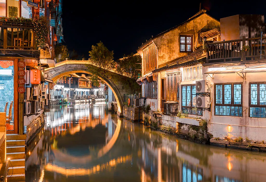 A scenic view of Zhujiajiao Water Town with traditional black-tiled roofs, old stone bridges over narrow canals, and wooden boats.
