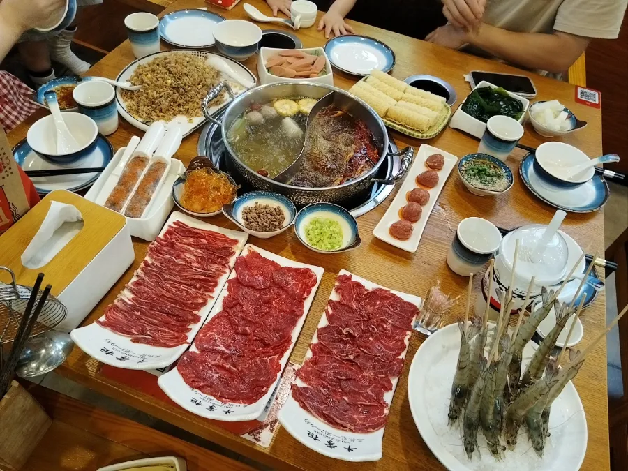 A simmering pot of clear beef broth surrounded by plates of freshly sliced beef at a Chaoshan hotpot restaurant in Shenzhen.