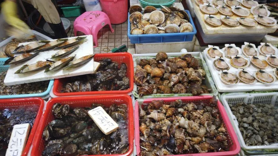 A lively seafood market stall in Shekou with plastic tubs of live crabs, prawns, and fish under bright lights.