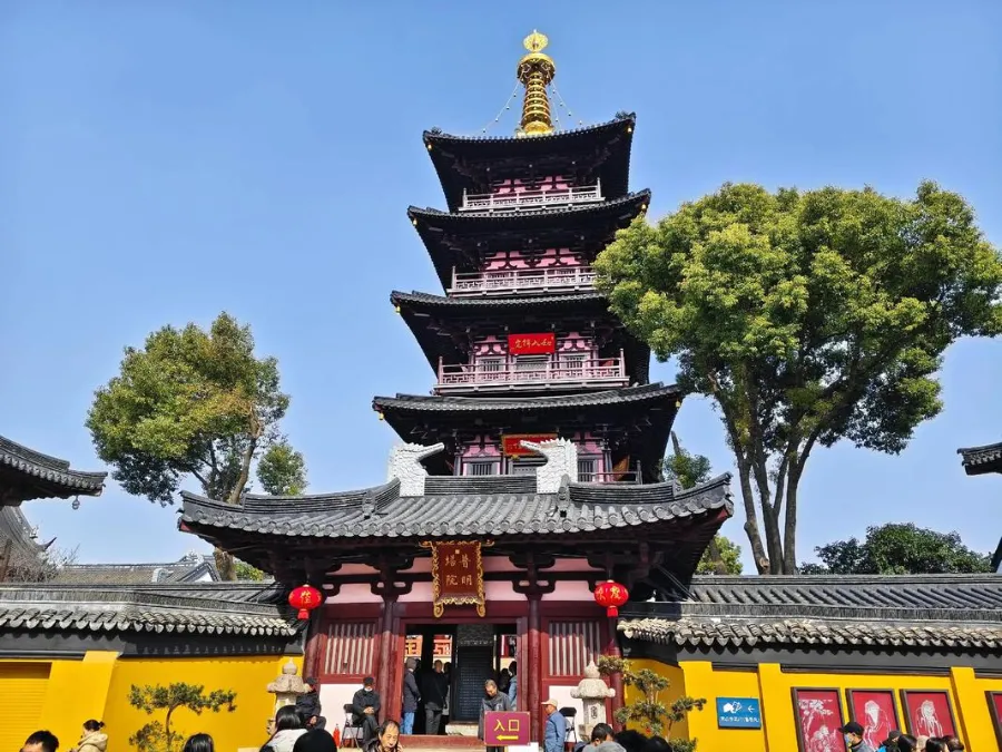 The yellow walls and traditional roof eaves of Hanshan Temple under green trees.