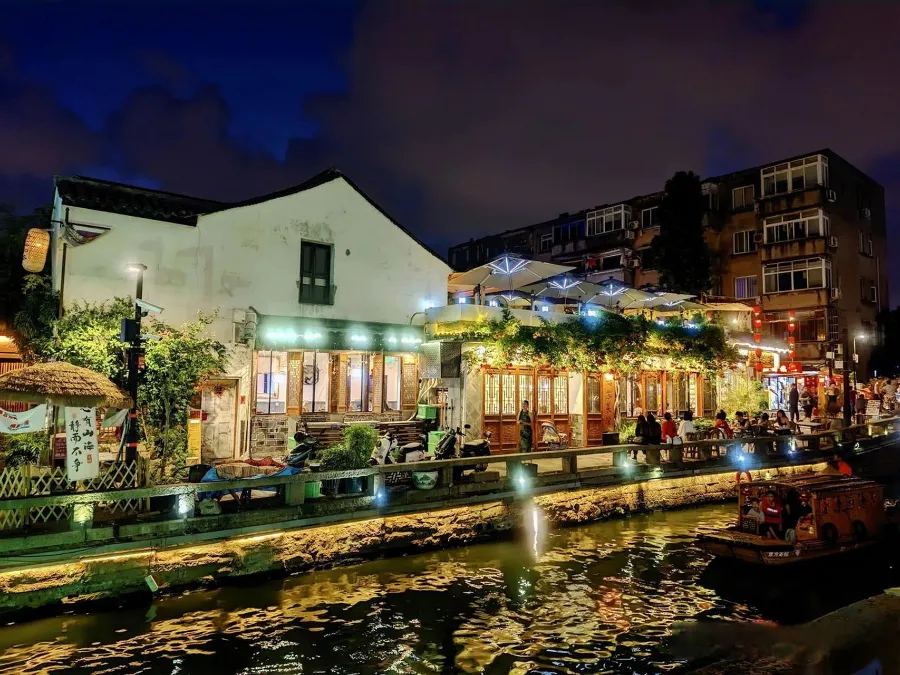 A narrow stone alley along the canal on Pingjiang Road in Suzhou with a small vendor selling hot snacks.