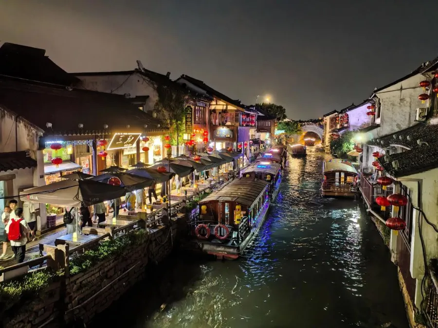 Traditional white-walled houses along the Shantang Street canal lit by red lanterns at dusk.