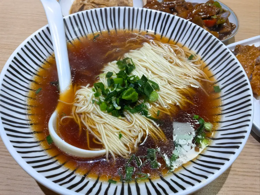 A bowl of neatly folded Su-style noodles in clear red broth topped with river shrimp.