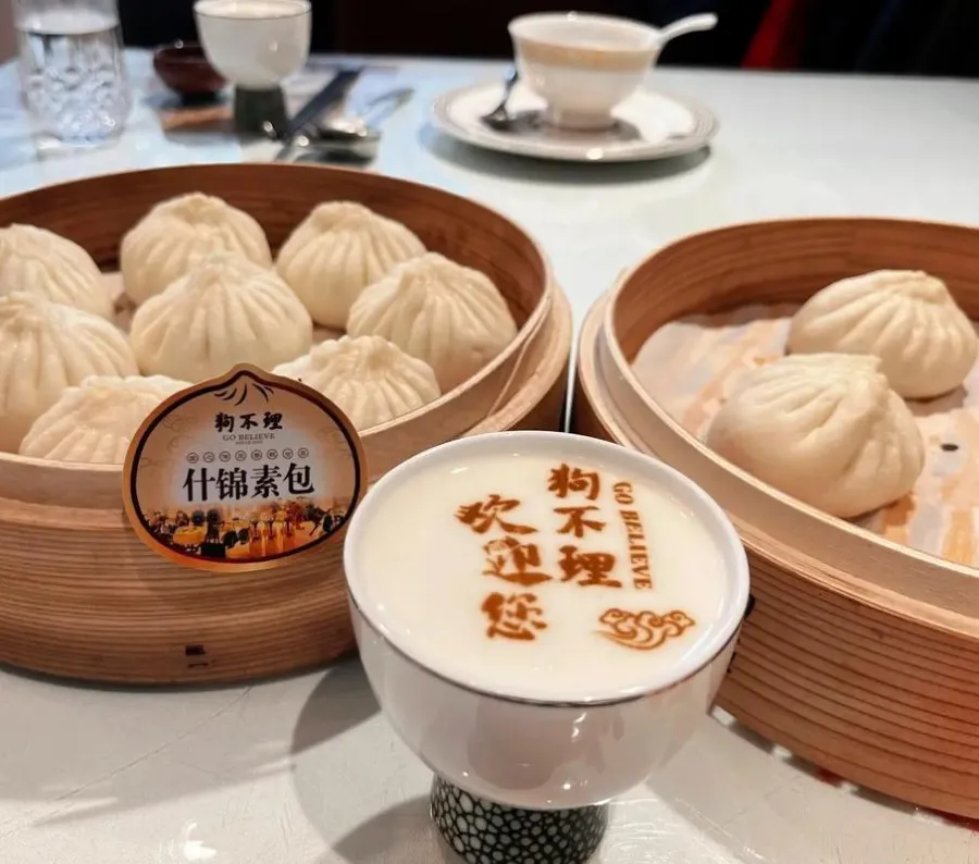 A steaming bamboo basket of freshly pleated pork baozi with a side of black vinegar and garlic.