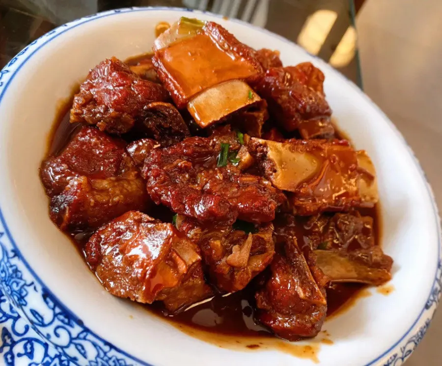 A platter of sticky, dark red-glazed Wuxi pork ribs garnished with green onions.