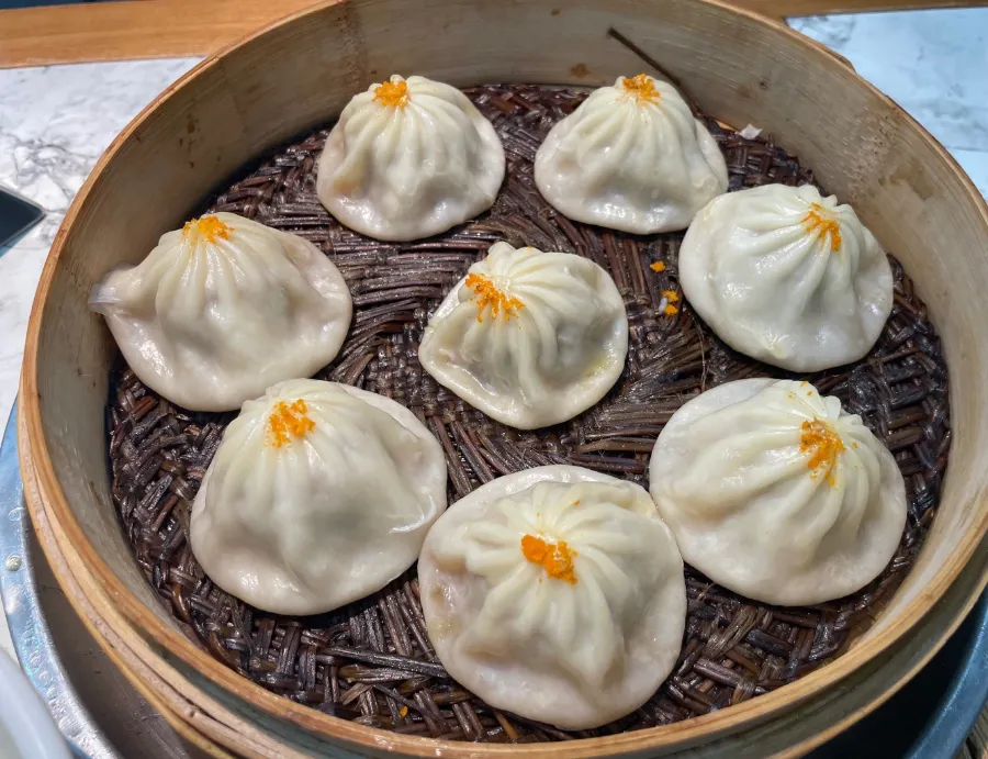 A bamboo steamer holding steaming Wuxi soup dumplings with glistening, thin skin.