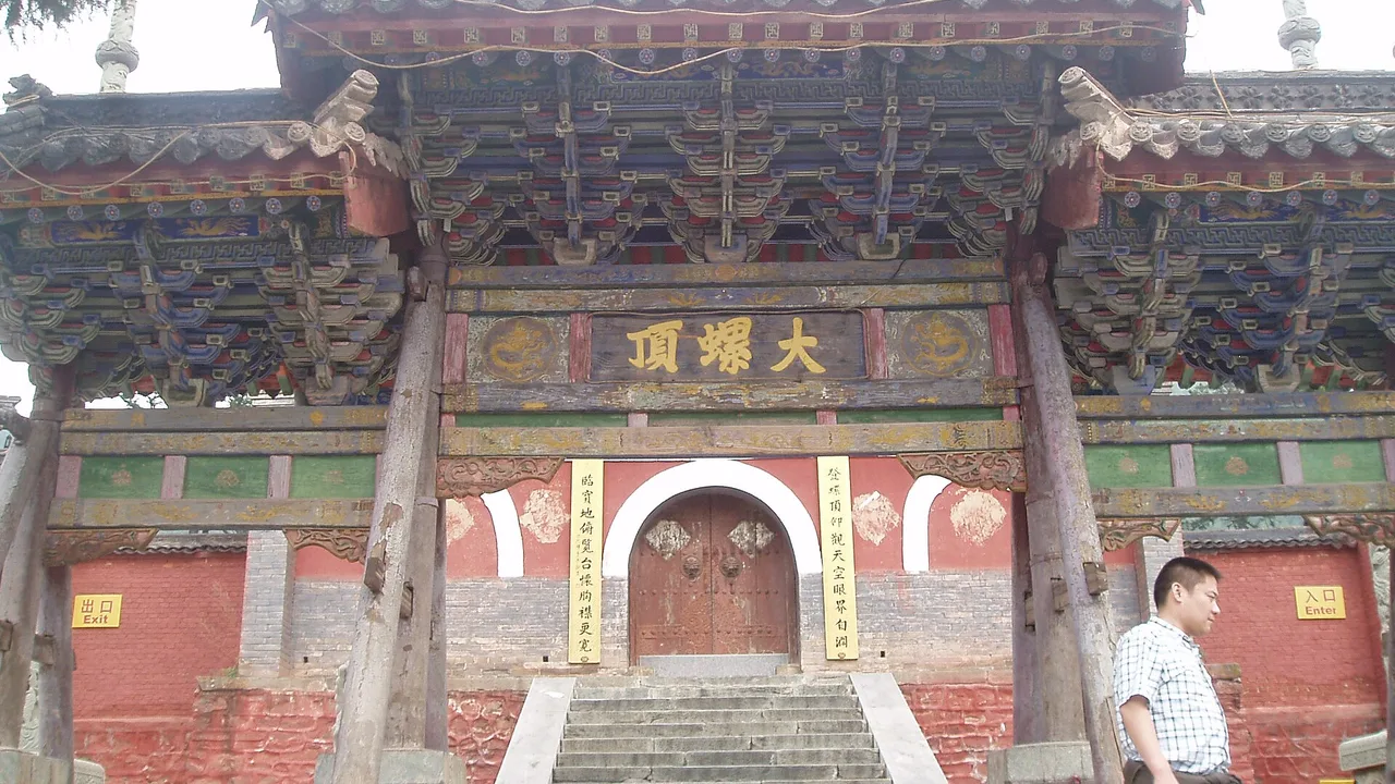 A temple gate with red walls, glazed-tile decoration and a carved plaque at Wutai Shan, the base of a three-day Xinzhou plan.