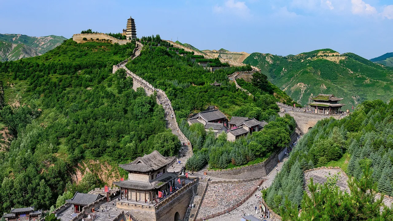 Yanmen Pass gate tower with Great Wall sections climbing green ridges on either side.