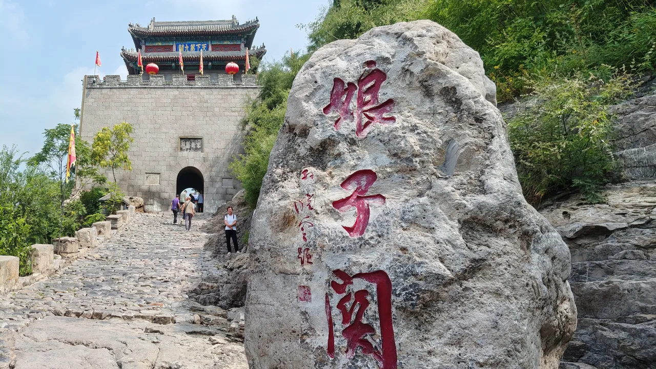 Stone path climbing to the gate tower of Niangzi Pass, beside a boulder carved with the pass's name in red characters.