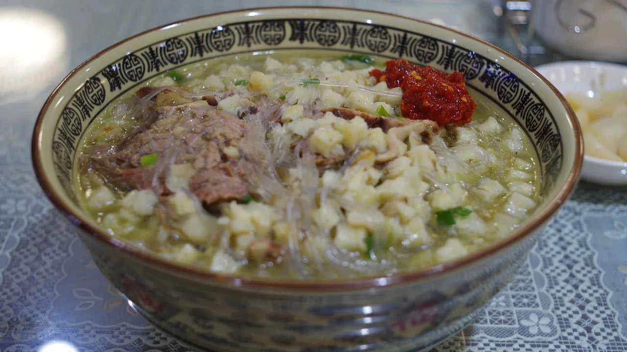 A bowl of mutton paomo with torn flatbread, mutton and chilli in milky broth.
