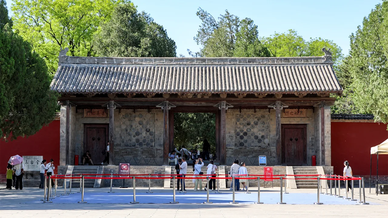 Yongle Palace in Ruicheng: a Yuan-dynasty gate hall with red walls and grey tile roof, trees behind.